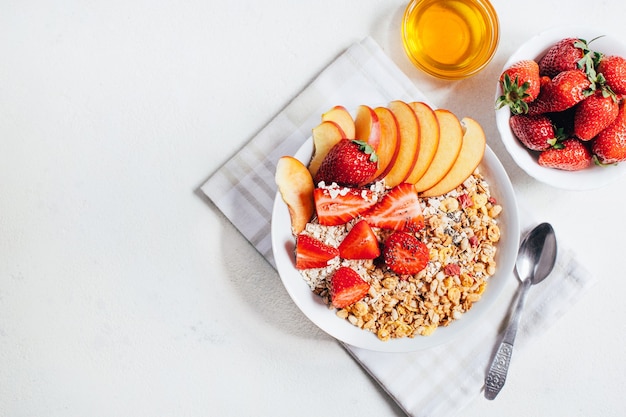 Top view of breakfast porridge oatmeal granola flakes dried fruits, strawberry, peach, honey on a white background