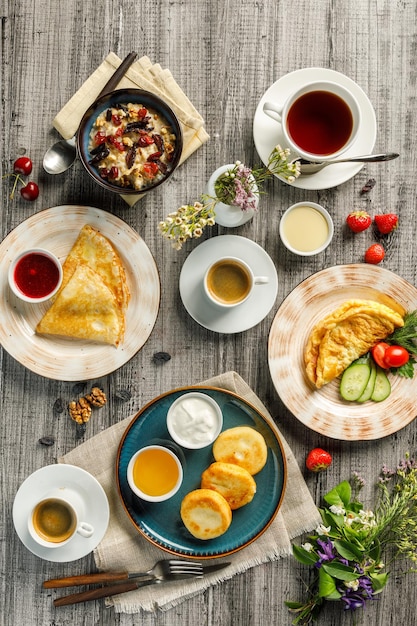 Top view of breakfast served with cottage cheesecakes omelette pancakes and porridge