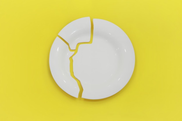 Top view on broken circle white plate on yellow background The plate broke into three pieces