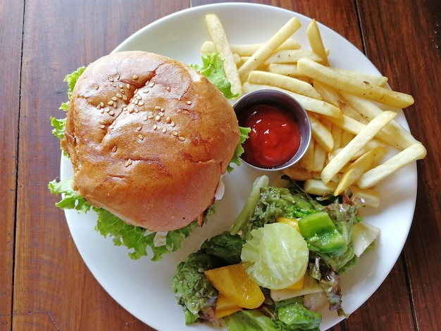 Top view of the Burger lying on a plate with a side dish of French fries and fresh salad, as well as ketchup