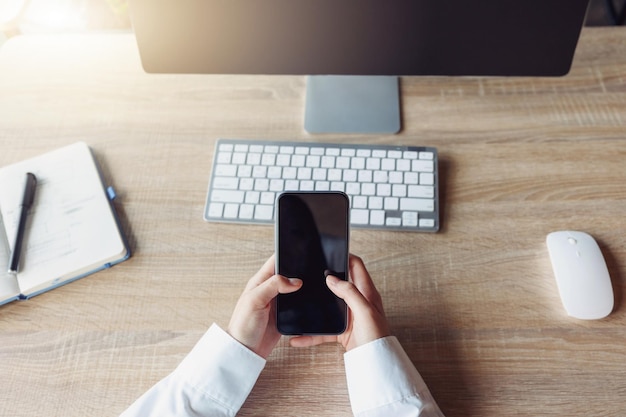 Top view of business woman hands holding phone while sitting in office on his workplace