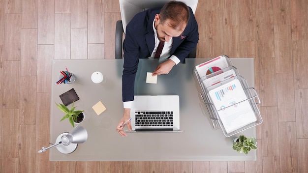 Top view of businessman putting stickey notes on laptop while working at company investments