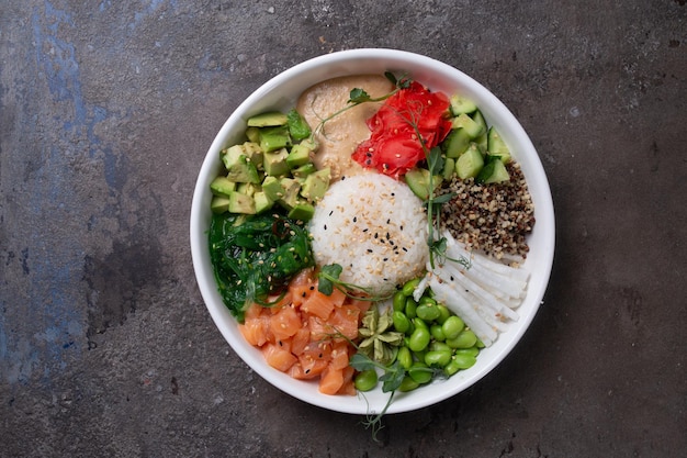 Top view of a bye bowl with salmon avocado cucumber sprouts and rice on a white plate