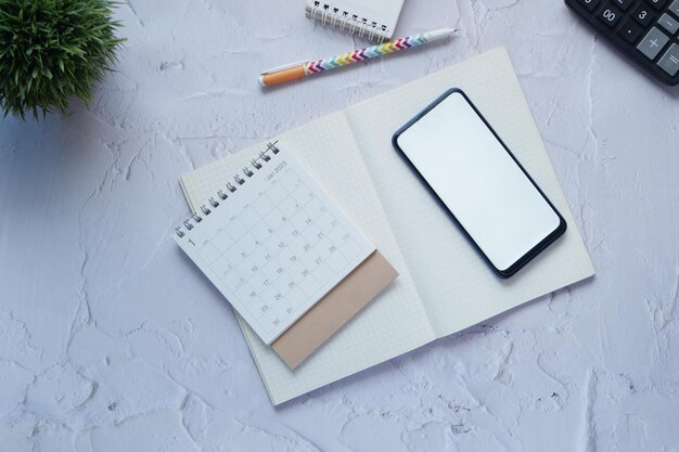 Top view of calendar and smart phone with white screen on table