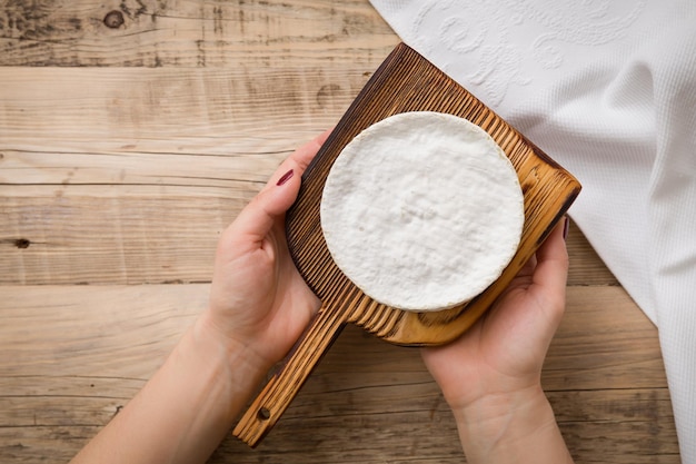 Top view on Camembert cheese on wooden board in woman's hands Serving French homemade soft cheese