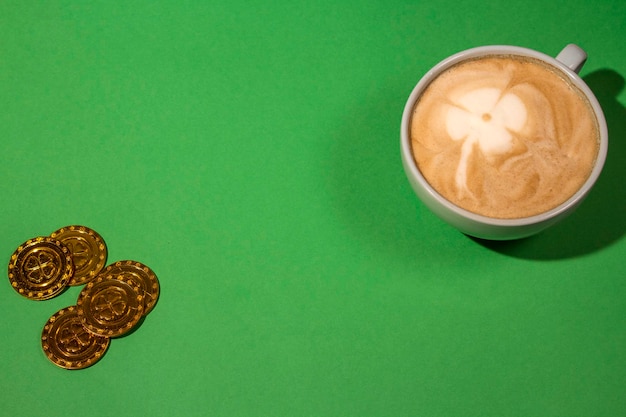 Top view cappuccino cup with four leaf clover on green background