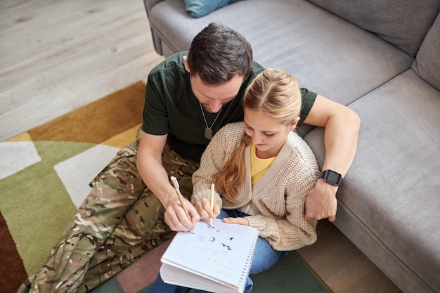 Top view of caring military father helping daughter doing homework