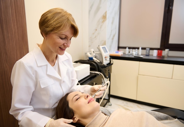 Top view of a charming middle aged woman relaxing in wellness spa clinic while getting facial dermabrasion treatment by a cosmetologist Skin care and beauty treatment concept