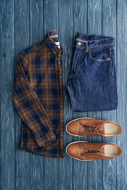 Top view of checkered shirt jeans and brown shoes on wooden background