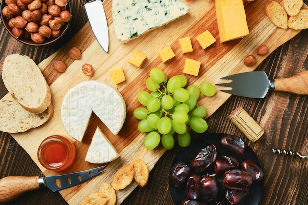 Top view of cheese plate with dorblu, brie, cheddar, grapes, honey, dates, crackers and nuts 