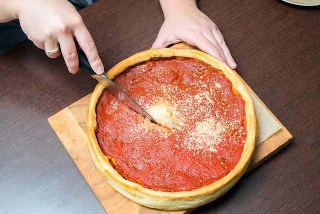 Top view of Chicago pizza. Woman hands cutting Chicago style deep dish italian cheese pizza with tomato sauce and beef meet inside