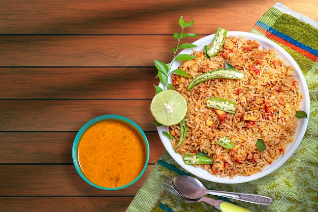 Top view of chicken fried rice with vegetables and chilli lime spoon and fork on a wooden table