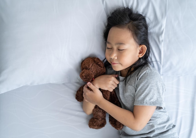 Top view child little asian girl sleeps in the bed with a toy teddy bear