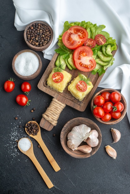 Top view of chopped and whole fresh vegetables on cutting board in bowls and spices on white towel on black surface