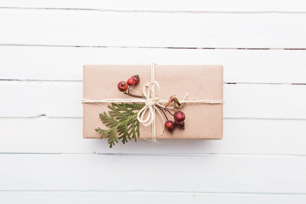 Top view on christmas gift wrapped in craft and decorated with various natural things on white wood