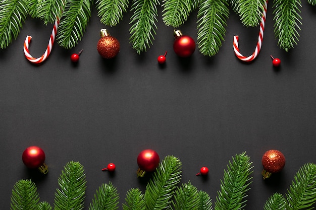 Top view of Christmas red balls with spruce  branches on black wooden background. Copy space.