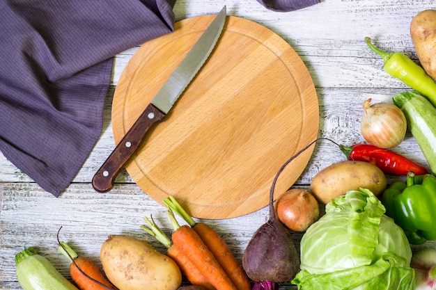 Top view of circle cutting board, knife and fresh vegetables on wooden table top