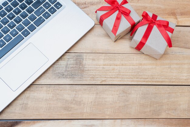 Top view close up gift boxes and laptop. Red ribbon bow with gift boxes on wooden table, Wrapped vintage box with copy space