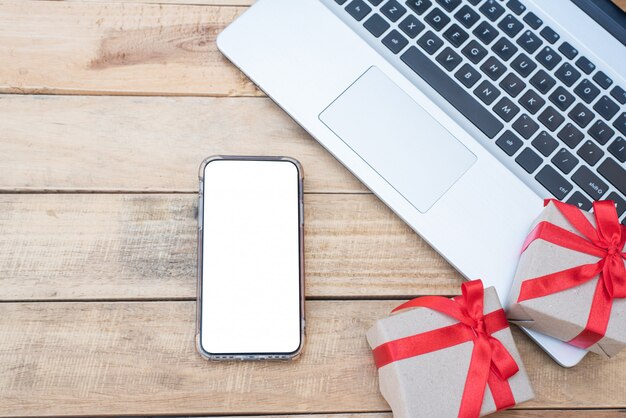 Top view close up gift boxes, smartphone and laptop. Red ribbon bow with gift boxes on wooden table, Wrapped vintage box with copy space