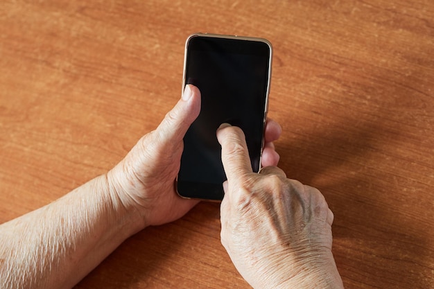 Top view close up of old woman's hand typing on smartphone