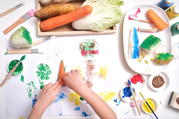 Top view close up of toddler boy child hands, kid making artwork from vegetable stamping at home