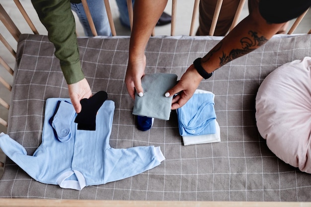 Top view closeup of couple expecting child and preparing crib with baby clothes copy space