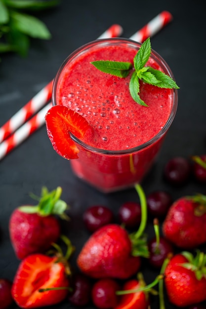 Top view closeup view of berry smoothie with fresh strawberries and cherries on black table