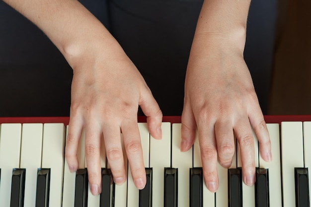 Top view closeup of a woman's hand playing a red electronic piano