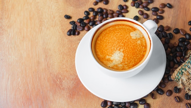 Top view of coffee cup has golden foam and mixed or blend coffee beans in a brown sack on wooden