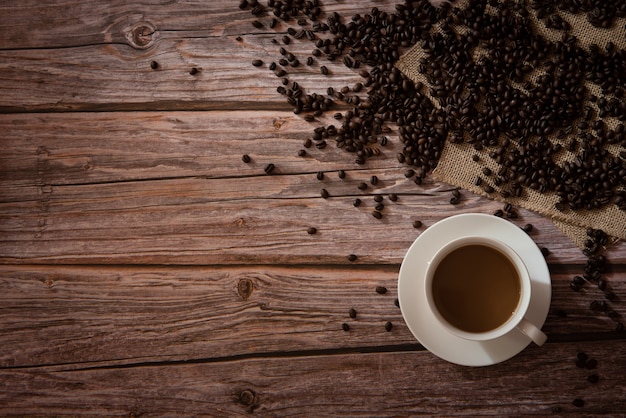 Top view of coffee in white cup and coffee beans on wooden background with copy space