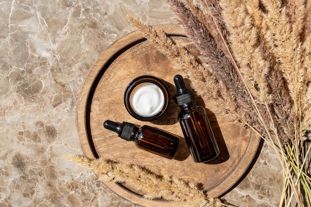 Top view of collagen cream in glass jar serum in amber glass bottle and dry flowers reeds on beige background Set for skin and body care beauty products