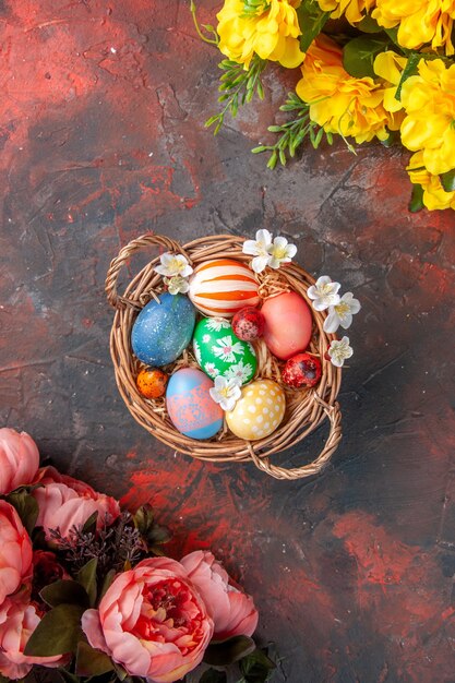 top view colored easter eggs inside basket with flowers on dark surface