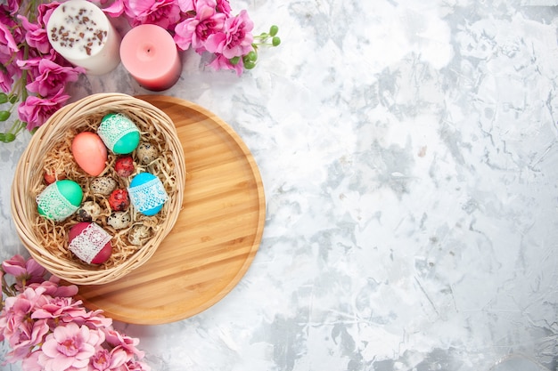 top view colored easter eggs inside basket with flowers on white surface