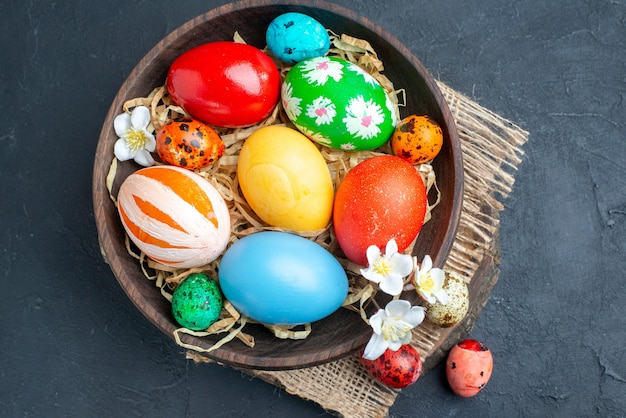 top view colored easter eggs inside plate with straw on dark surface