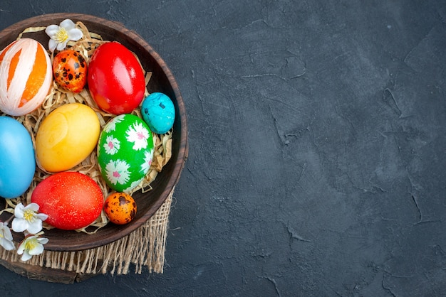 top view colored easter eggs inside plate with straw on dark surface