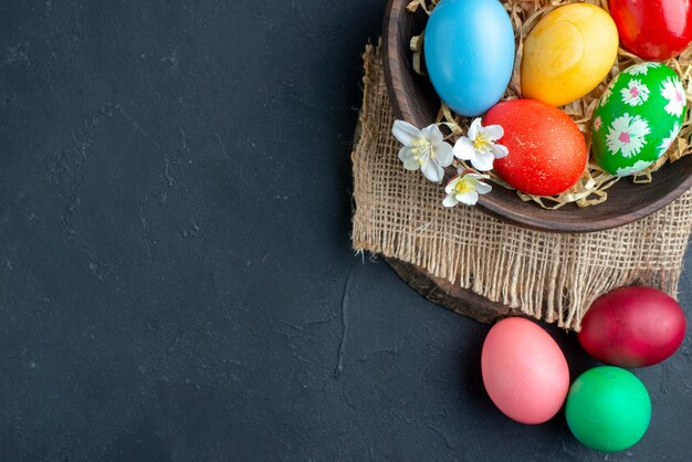 top view colored easter eggs inside plate with straw on dark surface