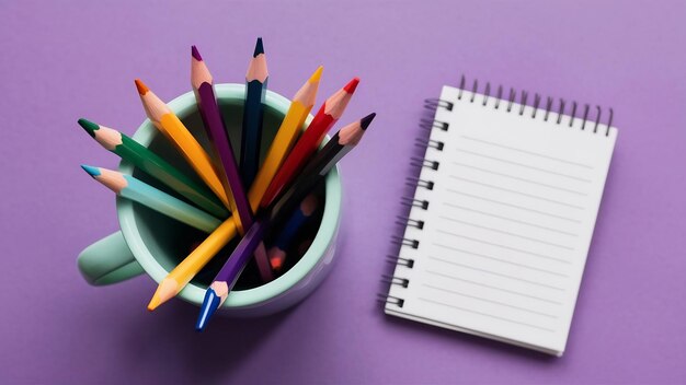 Top view of colored pencils in cup and note pad on purple background