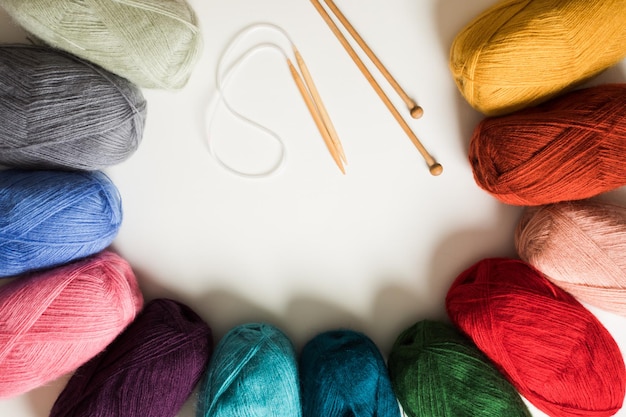 Top view of colored yarn balls and knitting needles on white