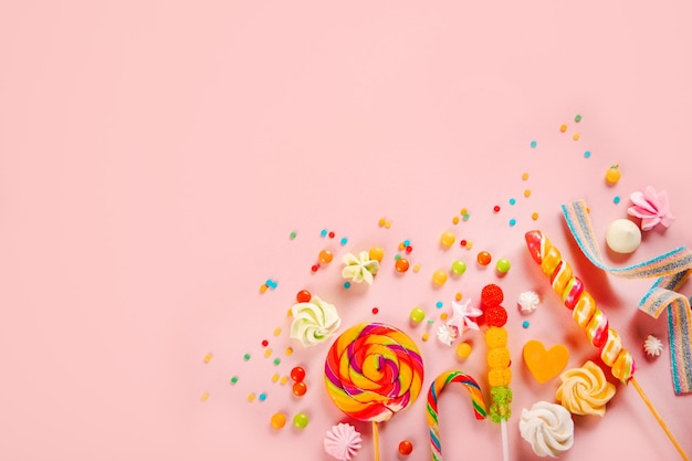 Top view of colorful candies and lollipops on pink background Copy space