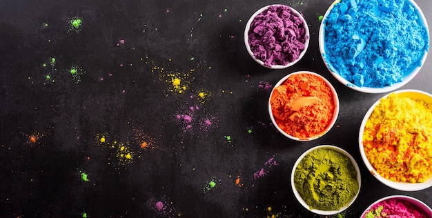 Top view of colorful holi powder with multicolored holi paint on dark background Happy holi festival decoration concept