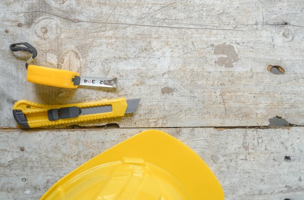 Photo top view construction tools such as a yellow hard hat spirit level measuring tape folding ruler arrayed against a wooden plank background