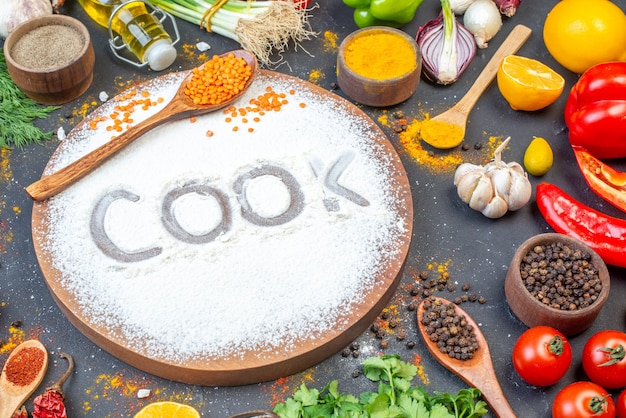 Top view of cook writing with flour on cutting board among fresh vegetables spices green bundles fallen oil bottle