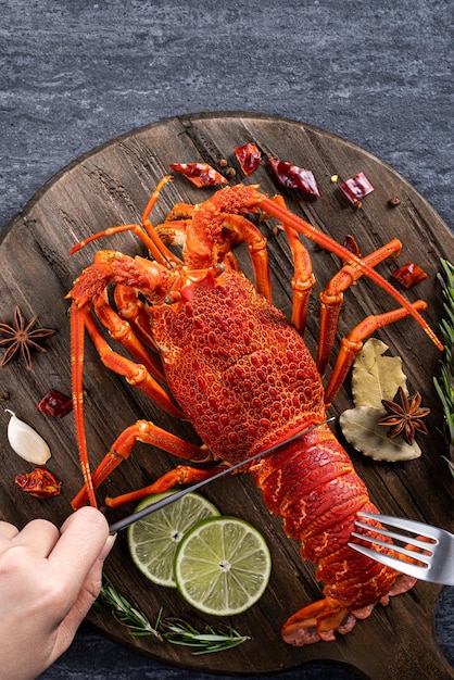 Top view of cooked boiled lobster, delicious dinner seafood meal set with knife and fork on black stone slate background for Valentine's day concept.