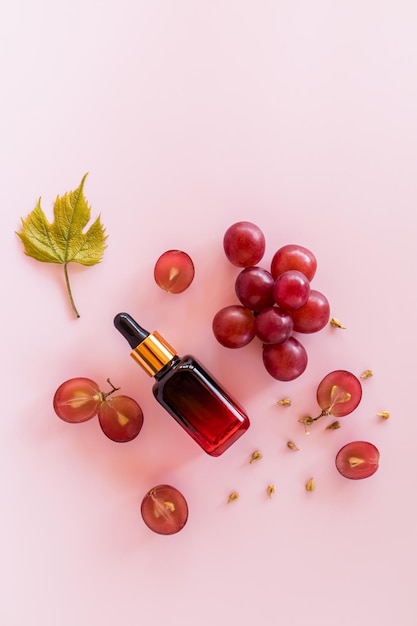 Top view of a cosmetic bottle with a pipette made of colored glass and ripe grape berries with organic natural cosmetics natural settlement