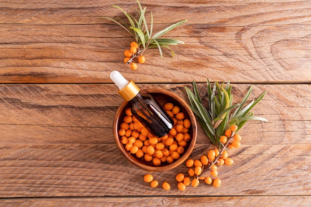 Top view of a cosmetic bottle with a sea buckthorn antiwrinkle agent in a bowl with sea buckthorn berries skin renewal wooden background