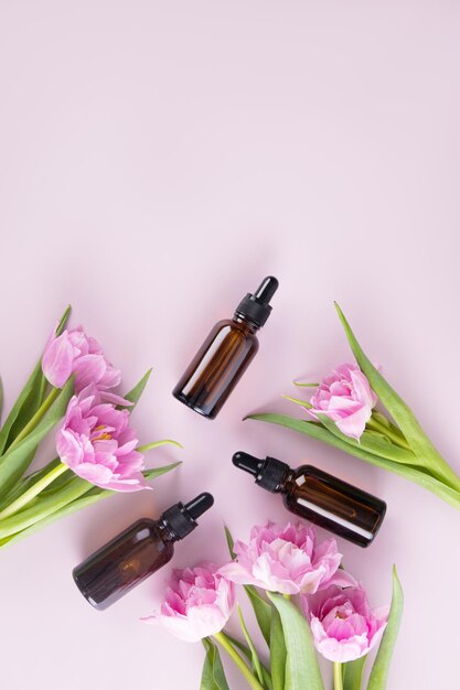 Top view of cosmetic bottles made of dark glass with a pipette with a natural facial skin care product Flat lay purple background spring flowers