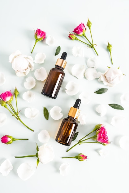 Top view of cosmetic bottles made of dark glass with a pipette with a natural organic facial skin care product rose petals and small roses Flat lay