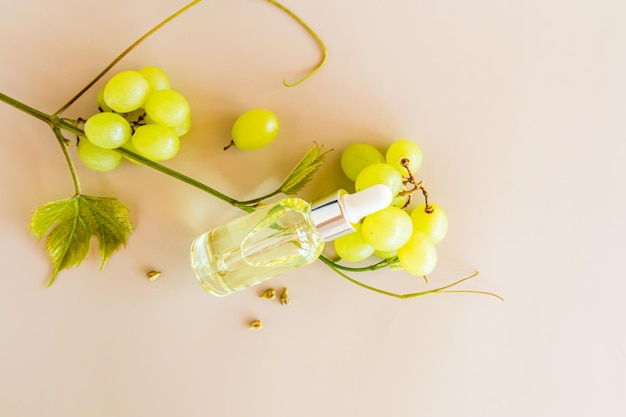 The top view of the cosmetic transparent bottle with organic product on the grape seeds lies on clusters of green grapes beige background