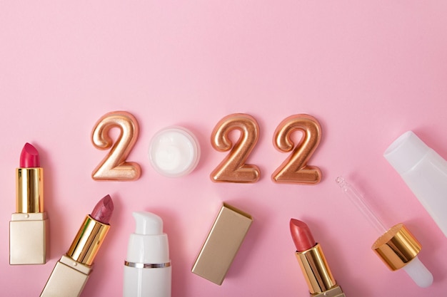 Top view of cosmetics containers and lipstick with numbers 2022 on pink background