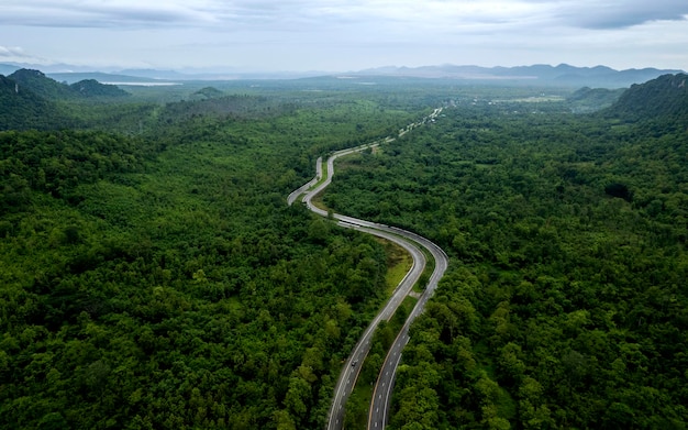 Top view of countryside road passing through the green forrest and mountain